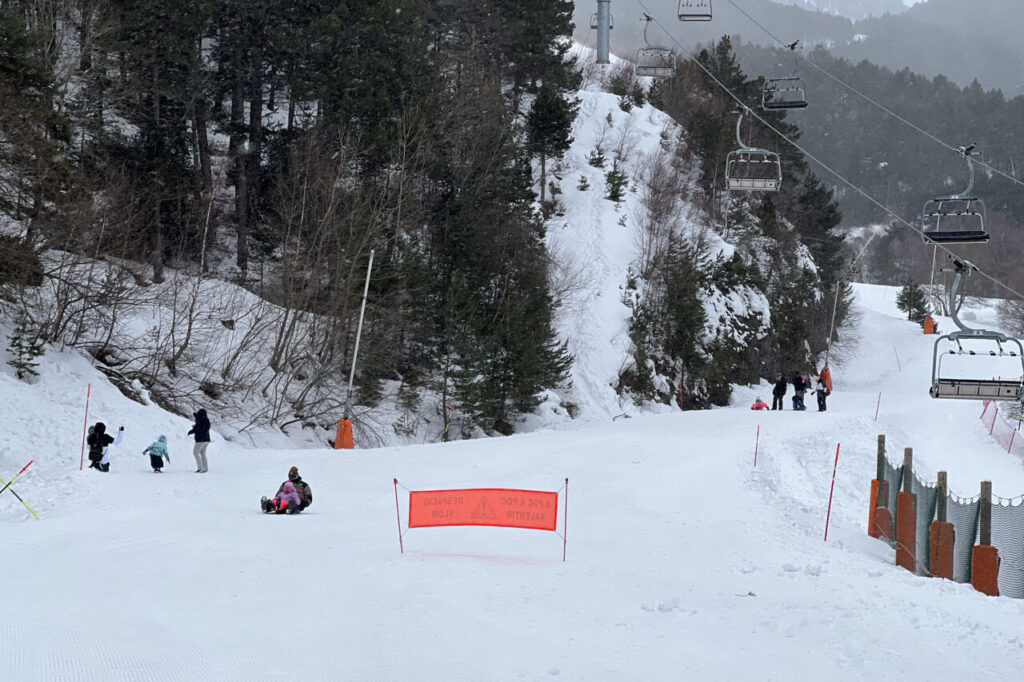 Diverses famílies gaudint de la neu a la base de l’estació d’Espot, que ha tancat pel vent i on es veu un telecadira buit i aturat (Albert L. Cobo, ACN)