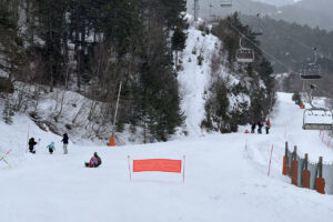 Diverses famílies gaudint de la neu a la base de l’estació d’Espot, que ha tancat pel vent i on es veu un telecadira buit i aturat (Albert L. Cobo, ACN)
