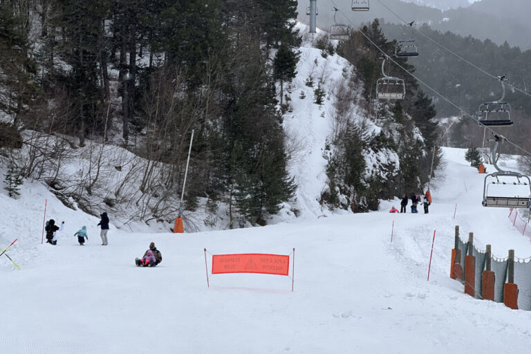 Diverses famílies gaudint de la neu a la base de l’estació d’Espot, que ha tancat pel vent i on es veu un telecadira buit i aturat (Albert L. Cobo, ACN)