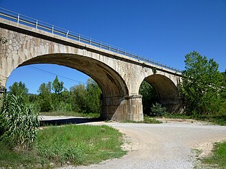 Pont de pedra de dos arcs amb barana metàl·lica, envoltat de vegetació.